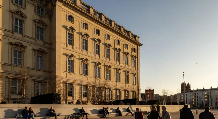 Sonnenlicht beleuchtet das barocke Gebäude, ein schönes Beispiel für kostenlose Orte, die man in Berlin besuchen kann. Menschen entspannen sich auf einer Bank.