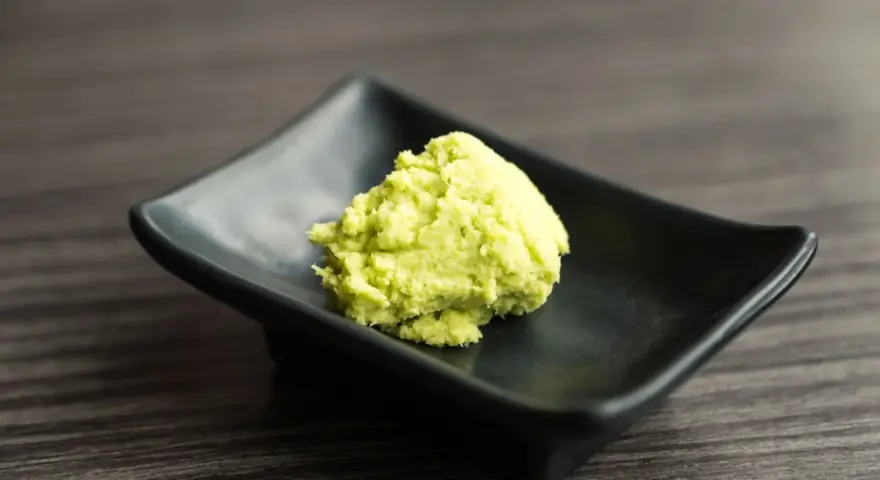 Zielona pasta wasabi na czarnej, kwadratowej miseczce. Zastanawiasz się wasabi co to? To ostry japoński chrzan.
