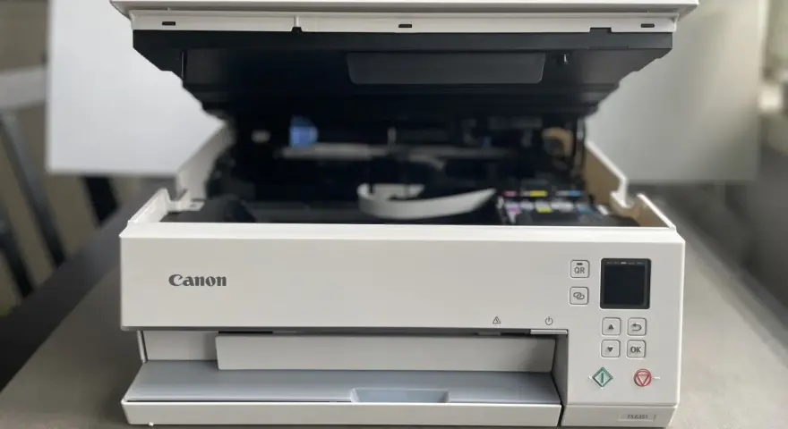 Biała drukarka Canon z otwartą pokrywą, widoczne tusze. Poradnik jak zainstalować drukarkę Canon.