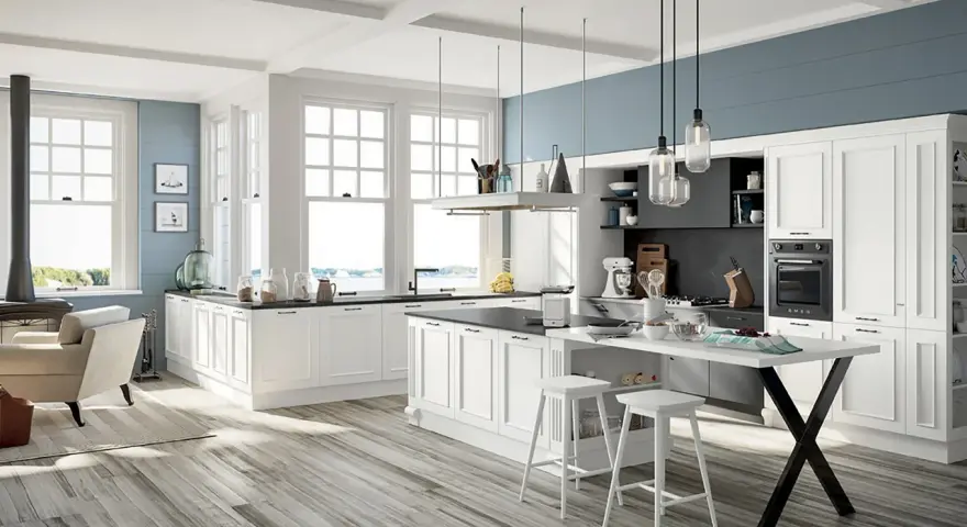 Cucina luminosa con isola centrale, sgabelli bianchi e una nicchia sotto finestra con vista mare.
