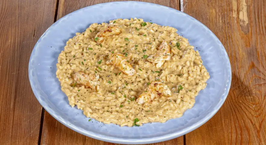 Un cremoso risotto alla crema di scampi, guarnito con scampi scottati e prezzemolo tritato, servito su un piatto azzurro.