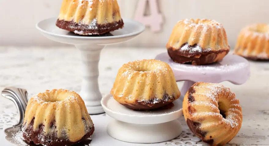 Mehrere mini Gugelhupf mit Puderzucker bestäubt, auf verschiedenen Etageren arrangiert.