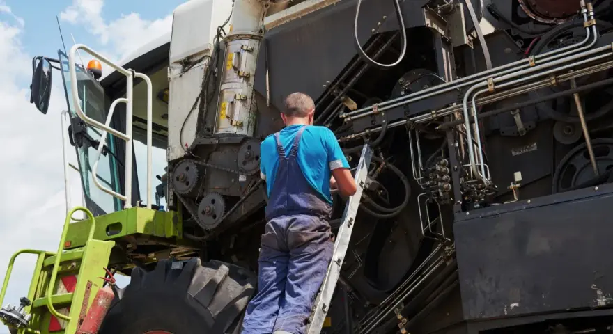 Mechanik na drabinie naprawia kombajn. Co to jest tuz? To potężna maszyna rolnicza, która zbiera plony.