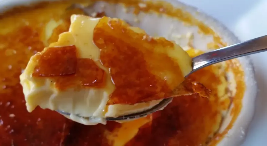 En sked tar en bit av en krämig creme brulee med karamelliserat socker. Perfekt dryck till creme brulee.