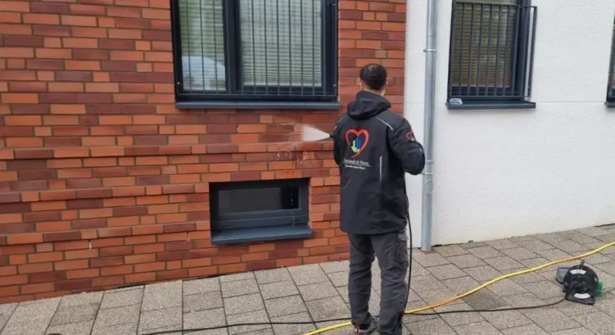 Mann reinigt mit Hochdruckreiniger die Ziegel-Fassade.
