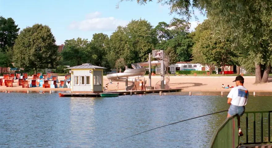 Am Orankesee Strandbad tummeln sich Badegäste, während ein Angler geduldig auf seinen Fang wartet.