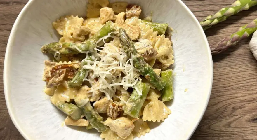 Pyszne makaron farfalle ze szparagami i kurczakiem w kremowym sosie, posypany startym parmezanem.