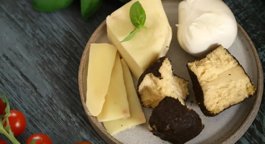 Różnorodne rodzaje serów na talerzu: kawałki żółtego sera, kulka mozzarelli i ser w ciemnej skórce.