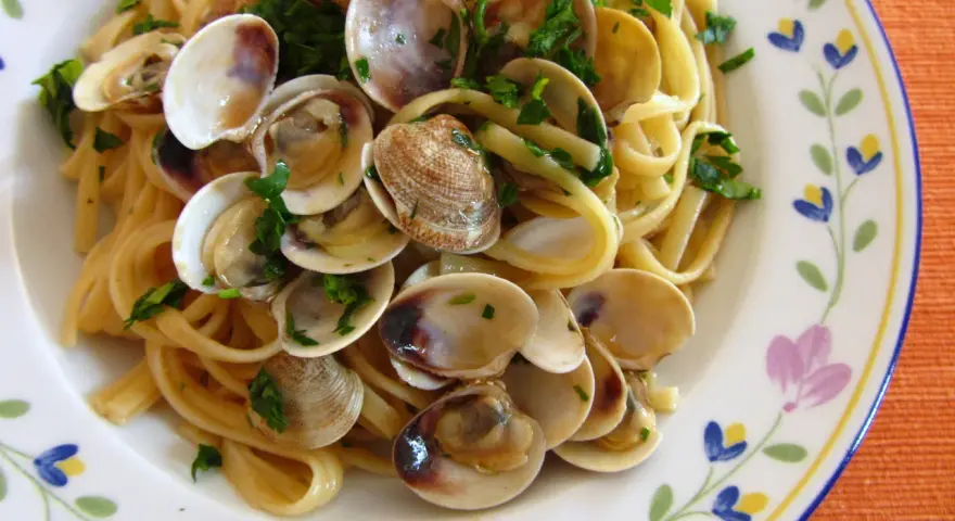 Pyszne spaghetti vongole z małżami i natką pietruszki na talerzu z kwiatowym wzorem.