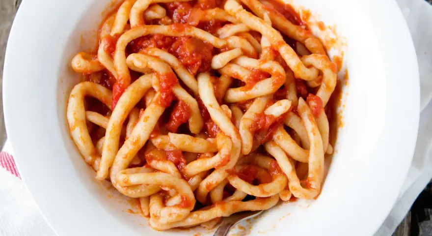 Piatto di pici fatti in casa conditi con un sugo rosso.
