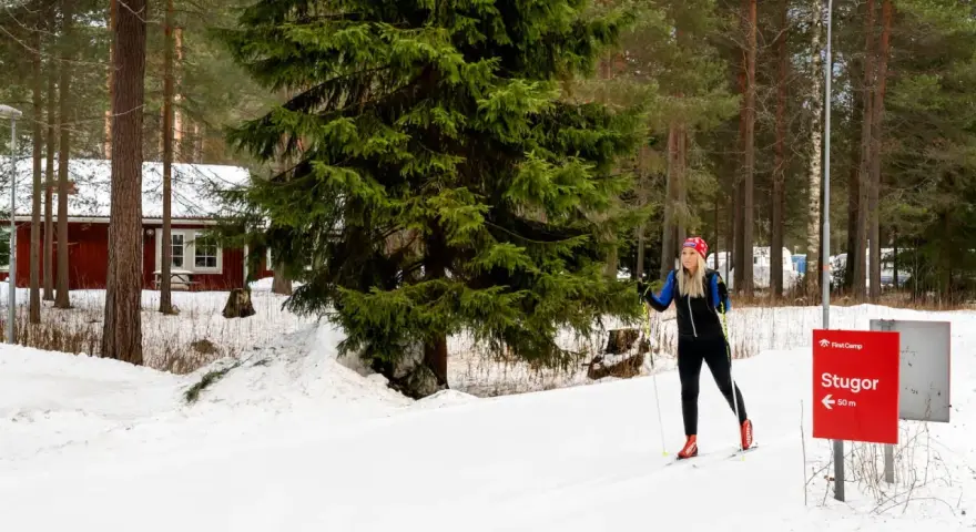 Kvinna på längdskidor vid Moraparken Camping. Röda stugor och granar i bakgrunden.