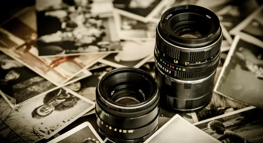 Dwa obiektywy aparatów leżą na starych, czarno-białych fotografiach.