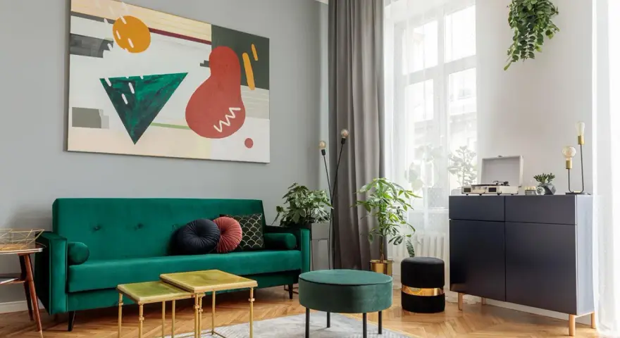 Soggiorno moderno con divano verde smeraldo e tavolini dorati. L'arte astratta sul muro grigio e i mobili scuri creano un perfetto abbinamento colori pareti e mobili.