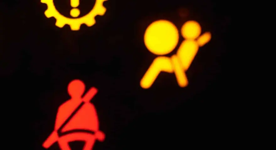 Das gelbe airbag symbol leuchtet. Daneben ein rotes Symbol für den Sicherheitsgurt. Ein gelbes Zahnrad mit Ausrufezeichen ist oben links zu sehen.