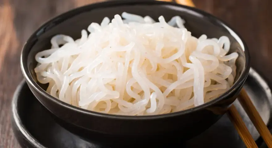 Misternie ułożony makaron konjac w czarnej misce, gotowy do spożycia z pałeczkami.
