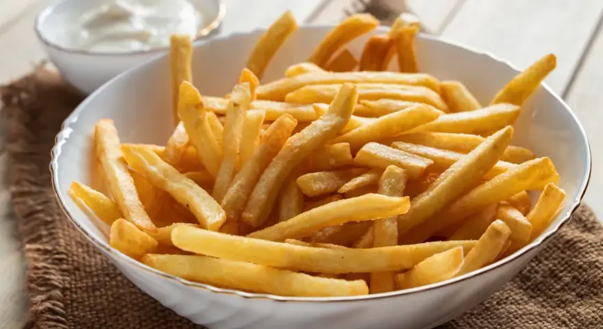 Chrupiące frytki z airfryer w białej misce, obok sos. Idealna przekąska na każdy dzień.