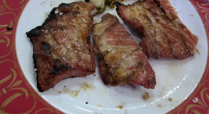 Tres trozos de secreto de cerdo a la parrilla, jugosos y con sal gruesa, servidos en un plato blanco con borde rojo.