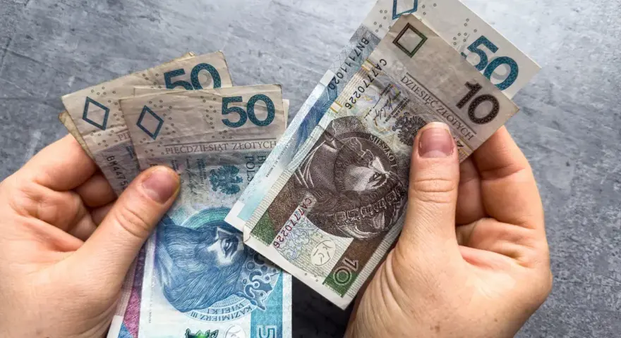 Dłonie trzymają polskie banknoty 10 i 50 zł. Może to symbolizować oczekiwanie na ponowne przeliczenie emerytury ZUS.