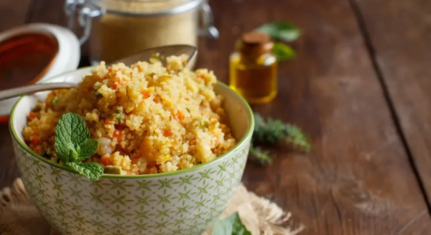 Schüssel mit buntem Couscous, garniert mit Minze. Daneben ein Glas Couscous und eine kleine Flasche Öl. Ein köstlicher Couscous-Baby-Genuss!