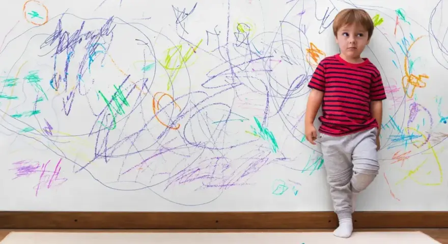 Chłopiec z ADHD, stojący przy ścianie pokrytej kolorowymi bazgrołami, wyraża swoje emocje.