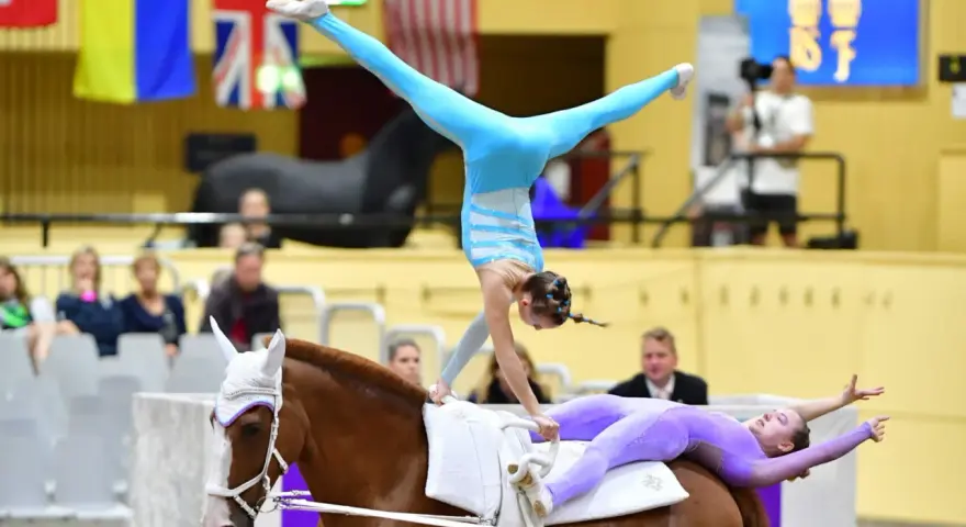 Deux gymnastes réalisent une performance de gymnastique cheval. L'une est en équilibre sur les mains, l'autre allongée sur le dos du cheval.