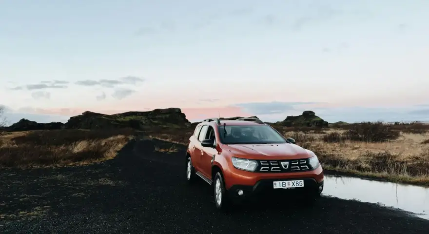 Pomarańczowy samochód na czarnej, wulkanicznej drodze. Islandia oferuje malownicze krajobrazy i swobodny ruch drogowy.
