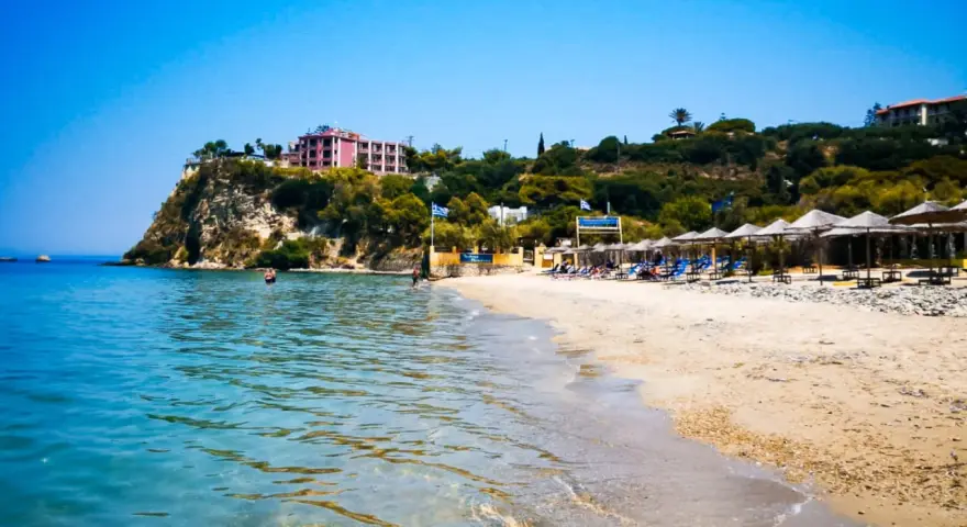 Piękne, turkusowe morze na Zakynthos. Plaża z leżakami i parasolami, a na klifie hotel.
