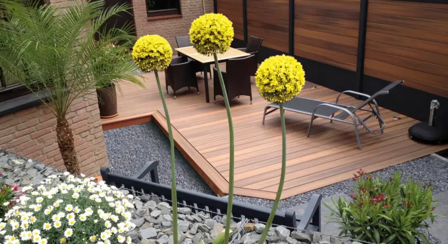Giardino moderno senza erba: deck in legno, ghiaia, piante in vaso e fiori bianchi. Esempi idee giardino senza erba.