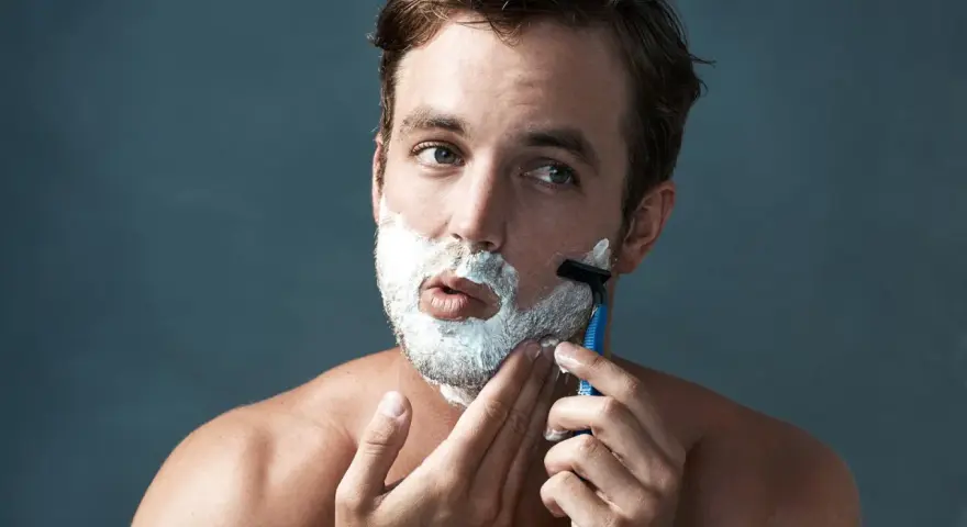 Hombre con espuma de afeitar en la cara, aprendiendo como afeitarse la barba con una maquinilla.