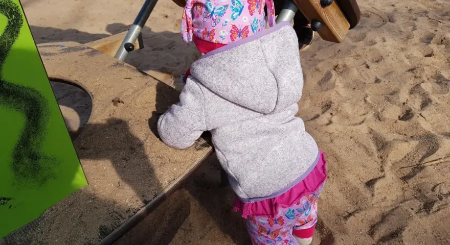 Kleines Kind auf dem Spielplatz, das die Welt erkundet. Manchmal sind die Nachteile der bindungsorientierten Erziehung, dass Kinder sich schwerer lösen können.