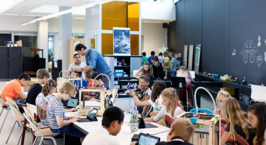 Children engage in 3d printing education, working with laptops and 3D printers in a bright, modern classroom.