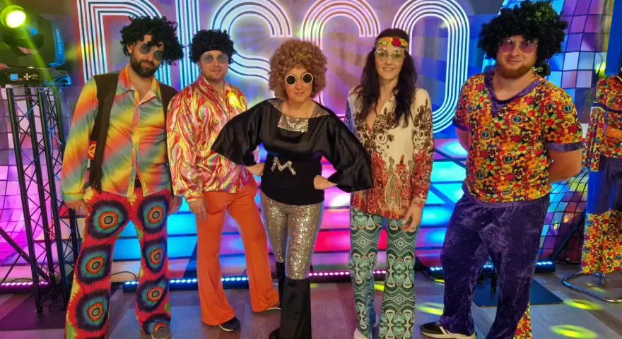 Pięć osób w kolorowych strojach disco z lat 70. na tle napisu "DISCO".