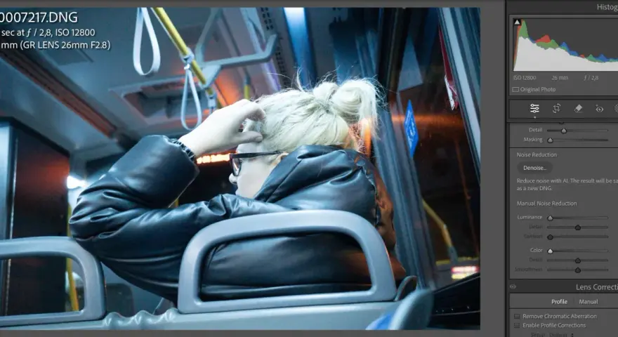 Kobieta w czarnej kurtce siedzi w autobusie, poprawiając włosy. Widać suwaki redukcji szumów w programie do edycji zdjęć.