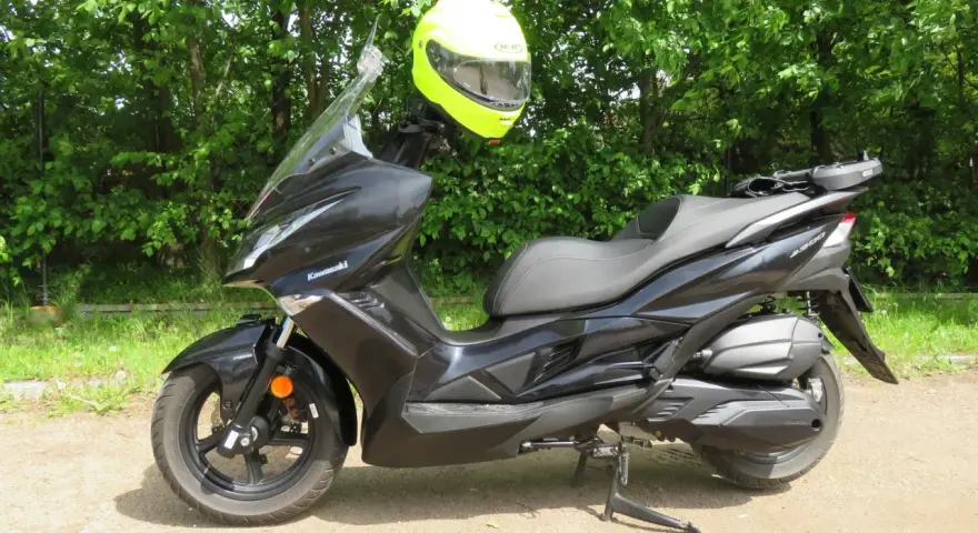 Czarny skuter Kawasaki J300 z jaskrawożółtym kaskiem zawieszonym na kierownicy, gotowy do jazdy w słoneczny dzień.