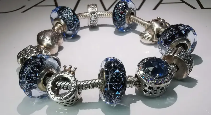 Bransoletka Pandora z niebieskimi szklanymi i srebrnymi charmsami. Zastanawiasz się, ile kosztuje naprawa bransoletki Pandora?