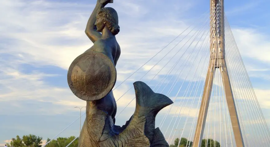 Syrenka Warszawska z mieczem i tarczą, symbol legendy o syrence warszawskiej, na tle nowoczesnego mostu.