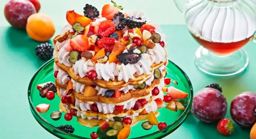 Eine beeindruckende Waffeltorte mit Erdbeeren und Mascarpone, geschichtet mit frischen Beeren und Früchten, auf einem grünen Teller.