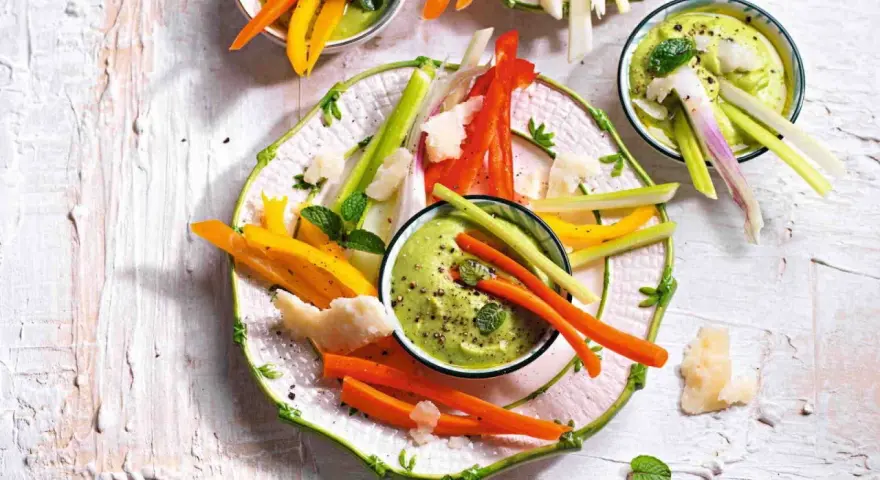 Deliziosi antipasti vegetariani: bastoncini di carote, peperoni e sedano con salsa verde cremosa, guarniti con scaglie di formaggio e menta.