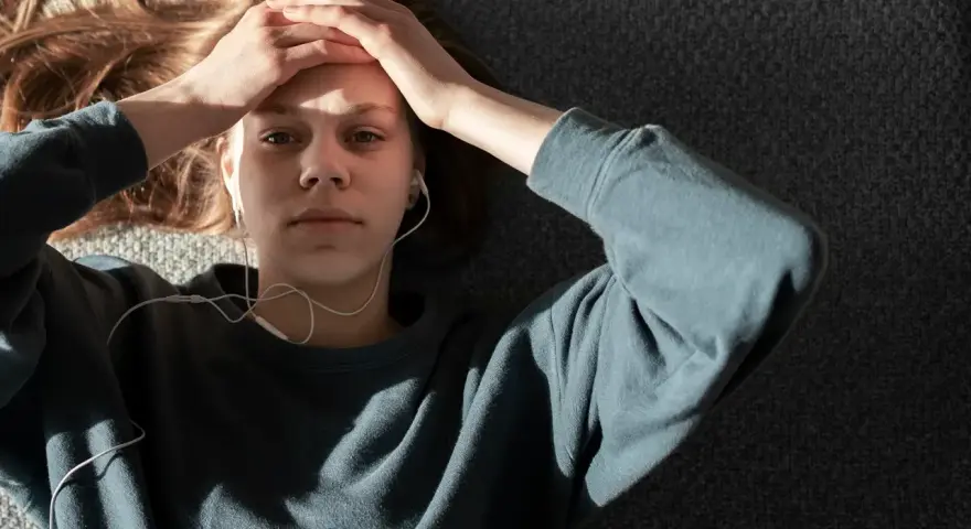En ung person med hörlurar ligger på en grå yta, med händerna mot pannan. Kanske lyssnar hen på musik för att få bort ångest snabbt.