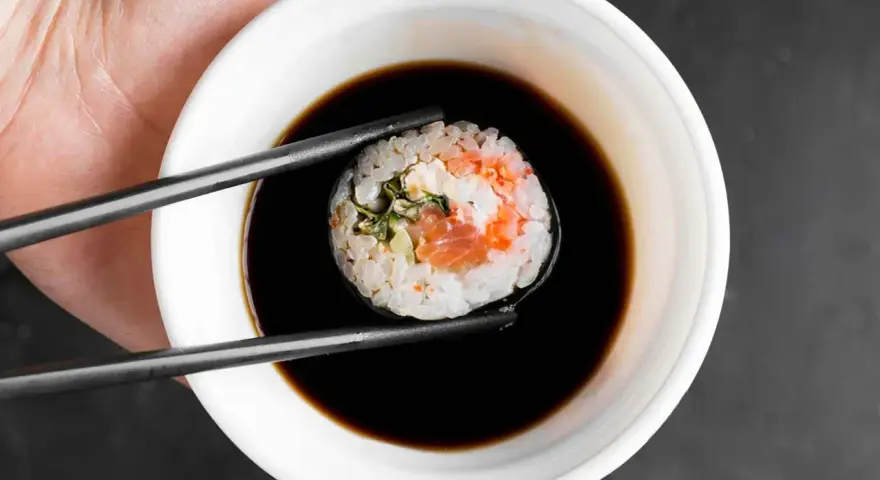 Pałeczkami zanurzam sushi w sosie do sajgonek. Widać kawałek łososia i ryż.