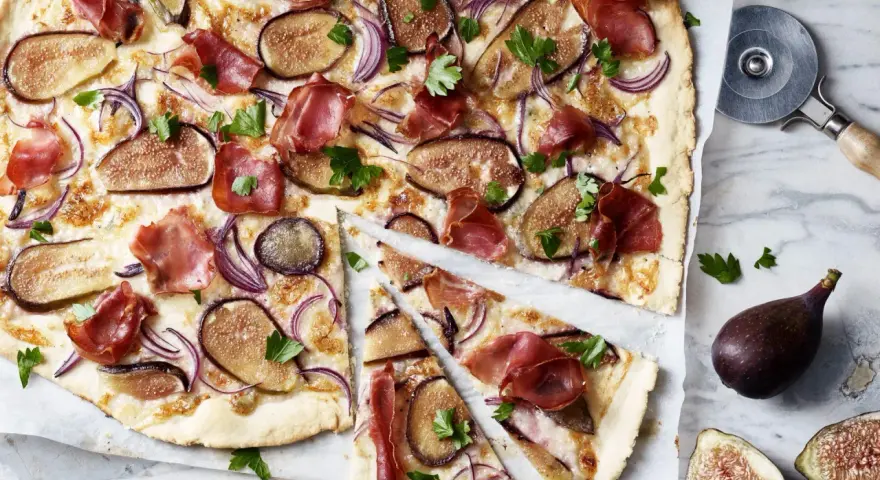 Ein köstlicher Flammkuchen mit Feigen, Schinken und roten Zwiebeln, garniert mit Petersilie.
