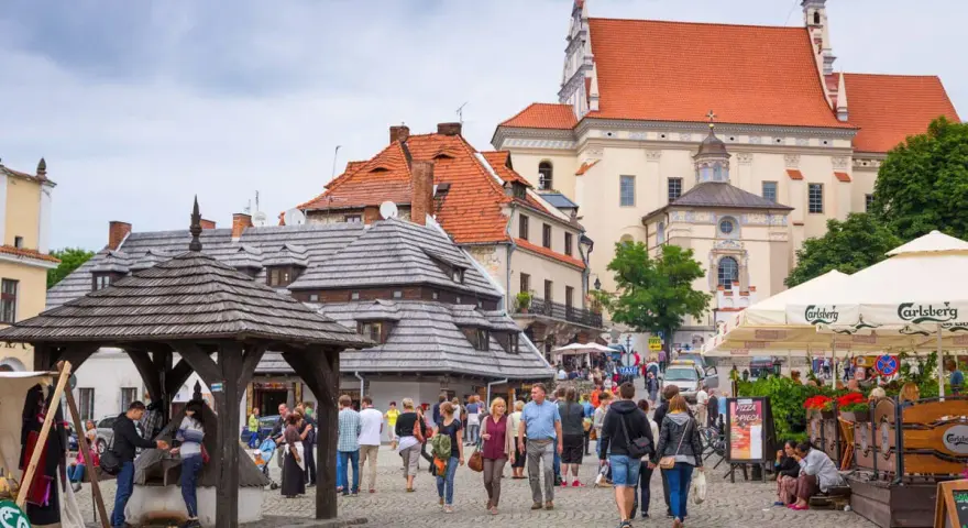 Tłum ludzi spaceruje po brukowanym rynku, podziwiając zabytkową architekturę. To urokliwe turystyczne miasta w Polsce.