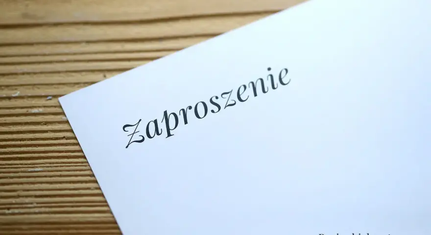 Eleganckie zaproszenie na ślub na białym, satynowym papierze, leżące na drewnianym tle.