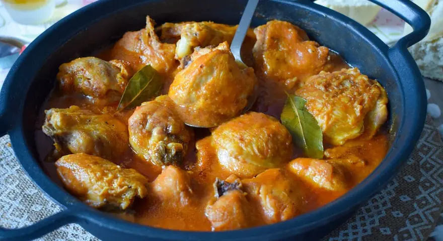 Sabroso pollo a la cerveza en cazuela negra, con salsa naranja y hojas de laurel.
