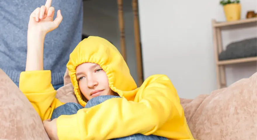 Ein Teenager in gelbem Hoodie zeigt seiner Mutter den Mittelfinger. Er hat keinen Respekt vor ihr.