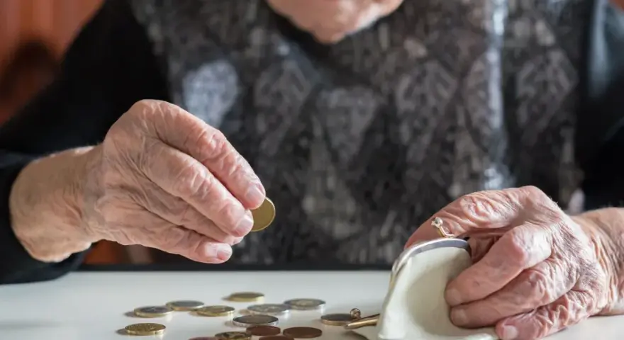 Dłoń starszej osoby liczy monety, zastanawiając się, kiedy najlepiej przejść na emeryturę w 2026 roku.