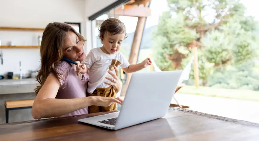Als alleinerziehende Mutter jongliert sie Arbeit und Kind. Sie telefoniert, während sie ihr Kleinkind hält und am Laptop tippt.