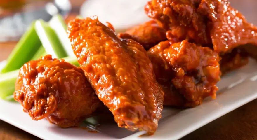 Alitas de pollo en freidora de aire, cubiertas de salsa picante, servidas con bastones de apio crujientes. ¡Un aperitivo irresistible!