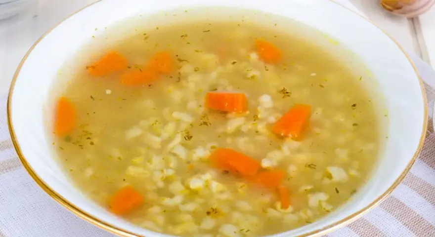 Aromaticzna zupa na rosole z makaronem i marchewką, podana w białej miseczce ze złotym rantem.