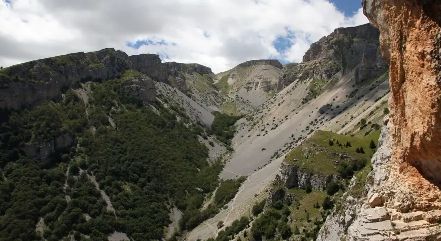 Un sentiero serpeggia tra montagne rocciose e vegetazione rigogliosa, un'avventura estiva al passo lanciano.